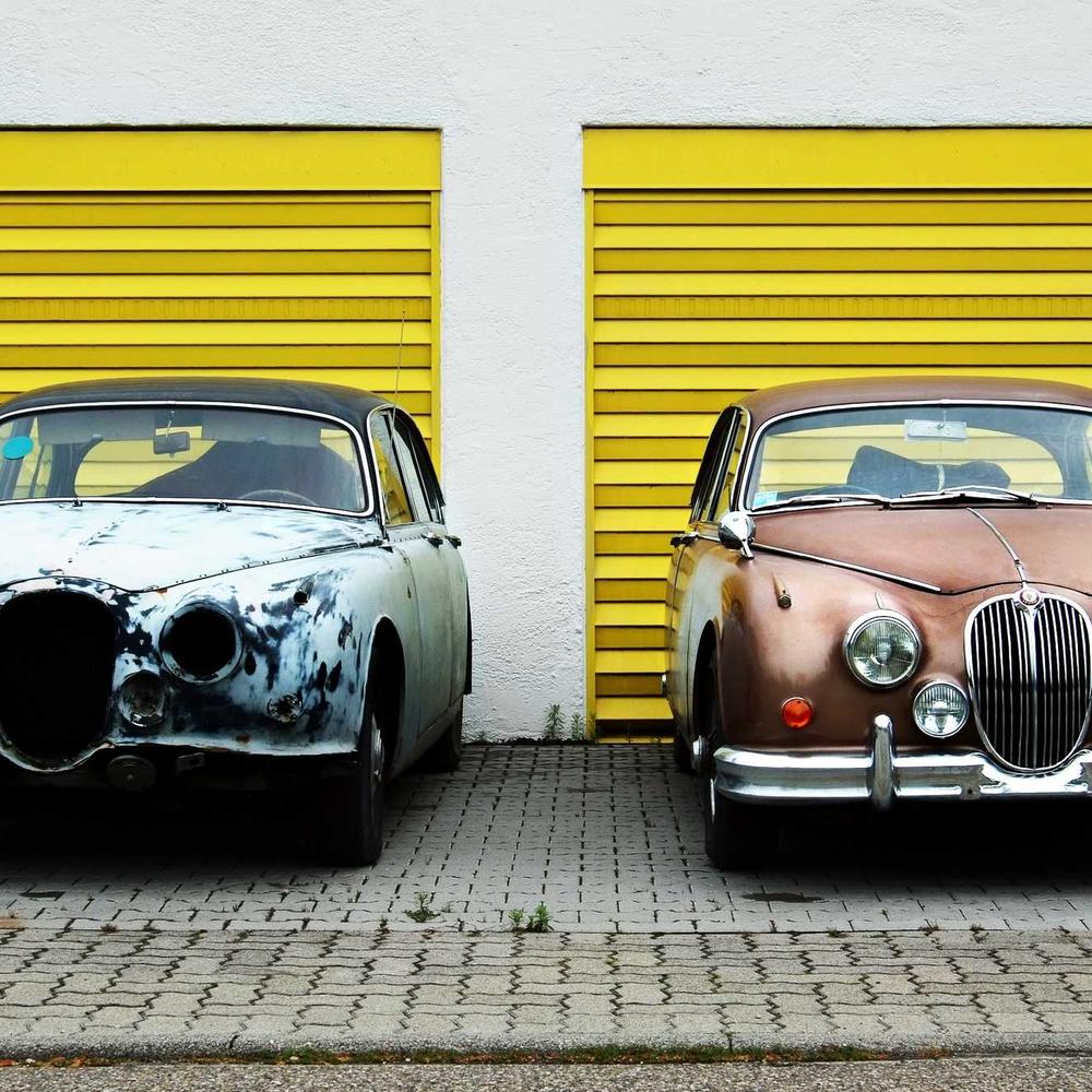 Two vintage cars parked by yellow garage doors